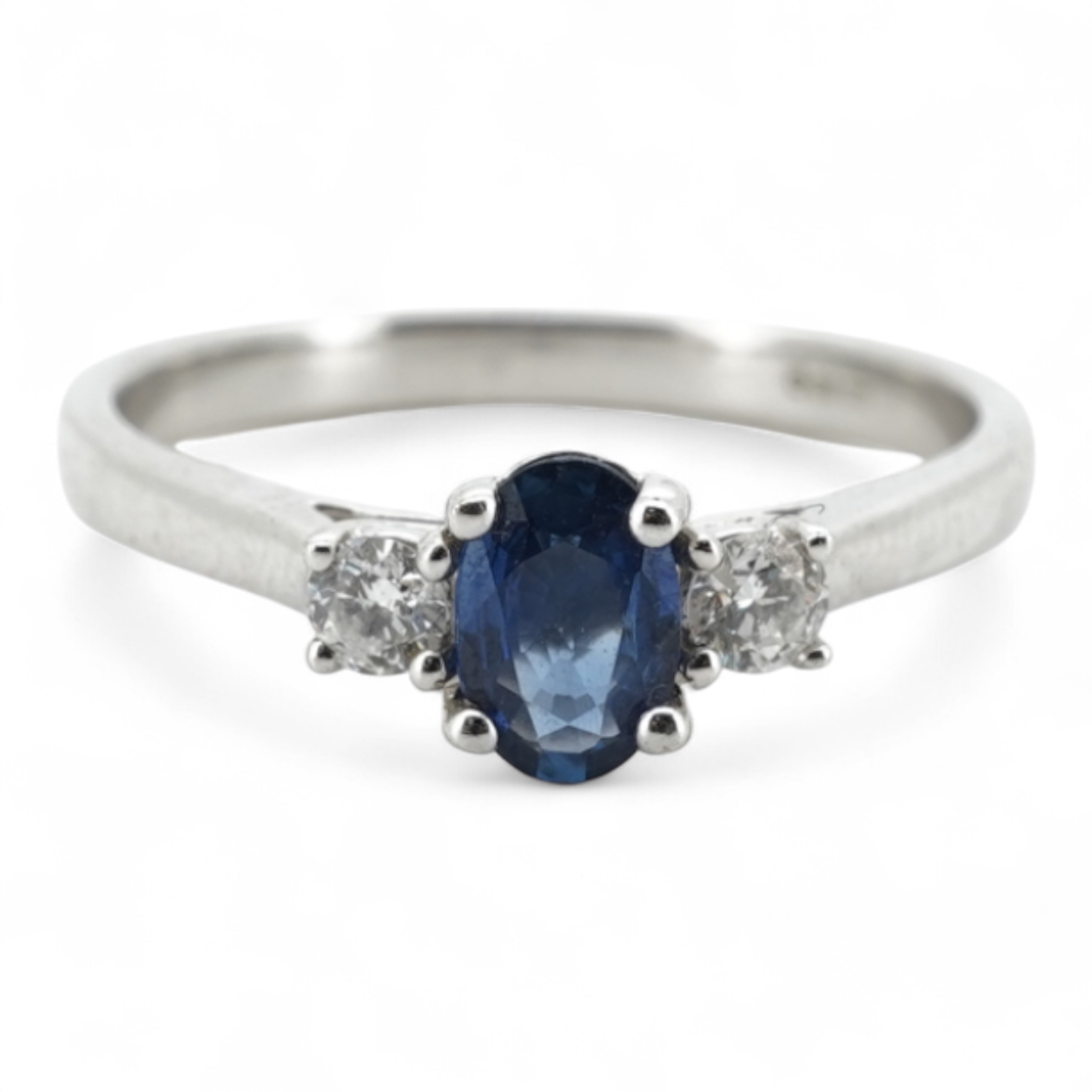 A sapphire and diamond three-stone ring, claw-set with an oval sapphire weighing approximately 0.35 carats, between shoulders set with brilliant-cut diamonds totalling approximately 0.12 carats, mounted in 9ct white gold